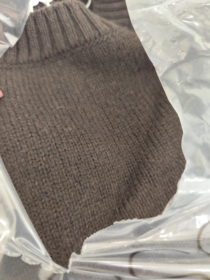 Κοντινό πλάνο στο γυναικείο πουλόβερ Philosophy Cashmere Round Neck μέσα στη συσκευασία του, στην απόχρωση Dark Brown, όπου διακρίνεται η πολυτελής πλεκτή υφή και η ριμπ λαιμόκοψη.