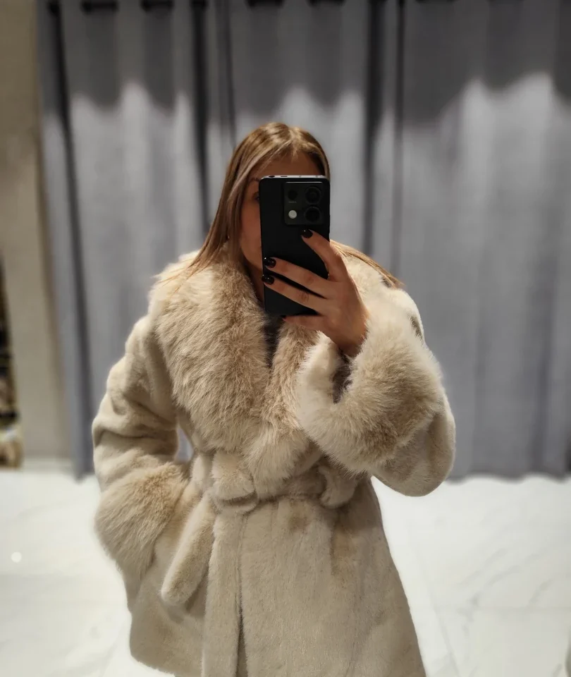 Mirror selfie του μοντέλου που φοράει τη δετή κοντή γούνα OUI ODILE Yara Corto σε κρεμ (burro) απόχρωση, με τα χέρια στις τσέπες
