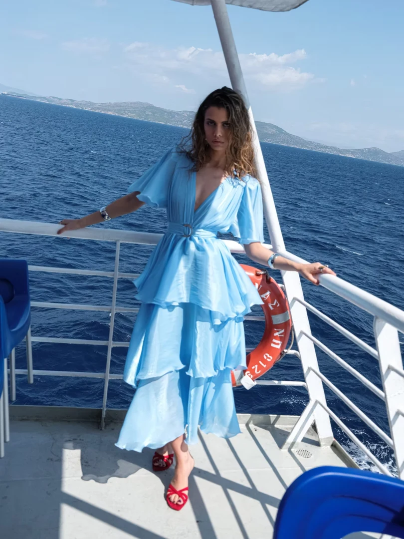 Ολόσωμη μπροστινή όψη με το μοντέλο να φοράει το γαλάζιο φόρεμα Nazezhda Sarah Dress Baby Blue από μεταλλική οργάντζα, αναδεικνύοντας το τριπλό βολάν.
