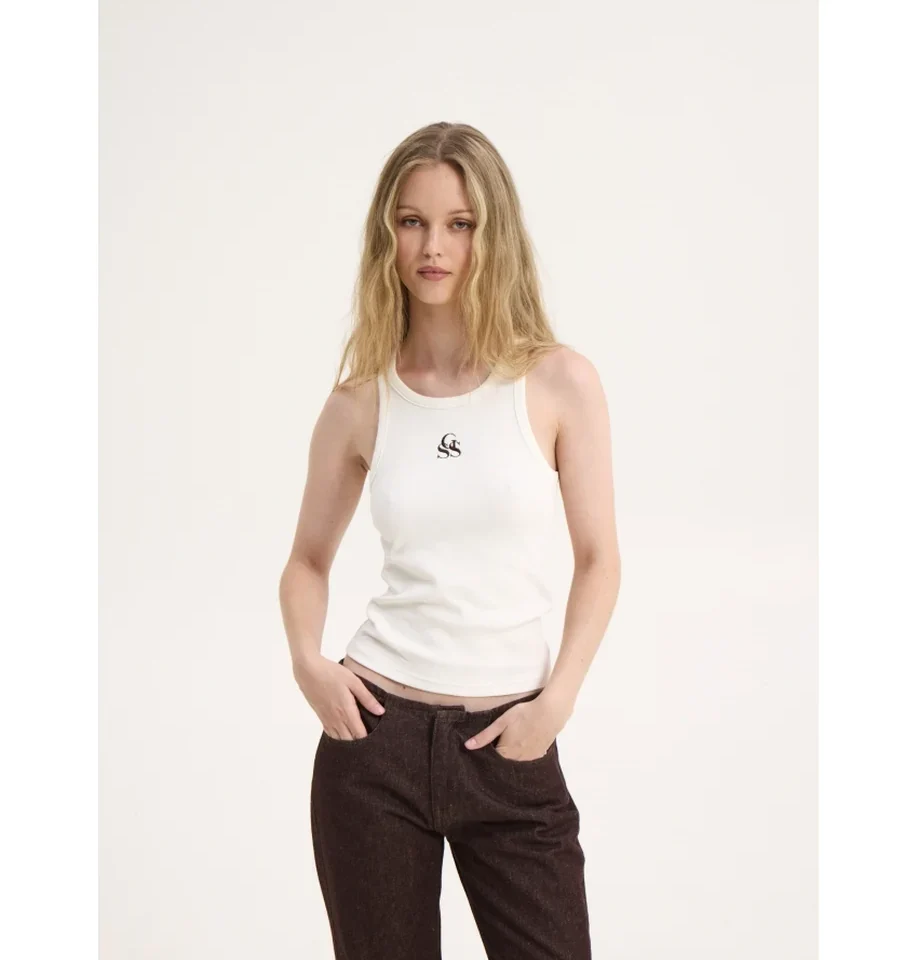 Μπροστινή λήψη του μοντέλου με το off-white τοπ SSG Tank Top της Sunsetgo, συνδυασμένο με καφέ τζιν παντελόνι