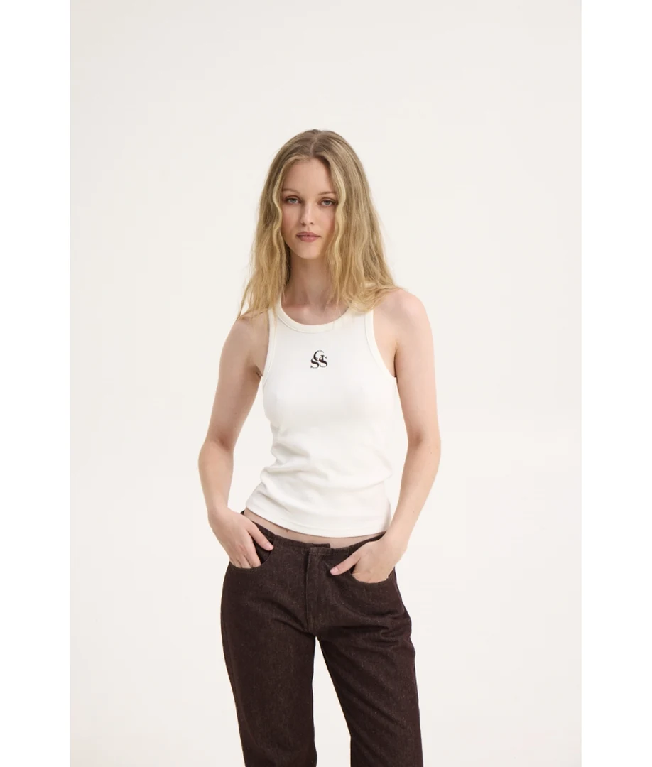 Μπροστινή λήψη του μοντέλου με το off-white τοπ SSG Tank Top της Sunsetgo, συνδυασμένο με καφέ τζιν παντελόνι